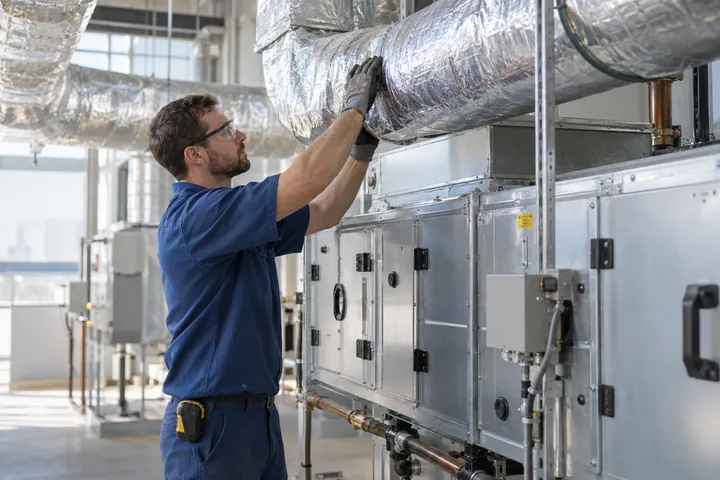 Technician fitting insulated ductwork beside a commercial air-handling unit
