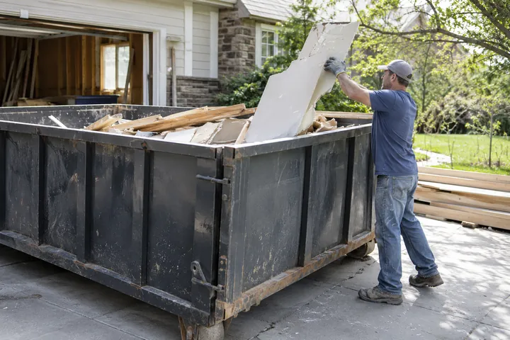 Worker placing renovation debris into a driveway dumpster